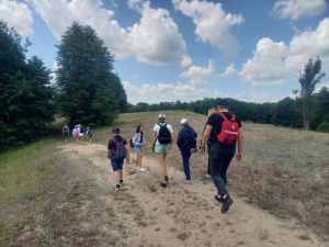 Grupa uczestników wycieczki maszerująca wzdłuż wydmy i skrajem lasu na Grzędach.