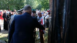 Grupa mężczyzn zdejmuje wspólnie szarfę z pomnika pamięci mieszkańców wsi Grzędy.