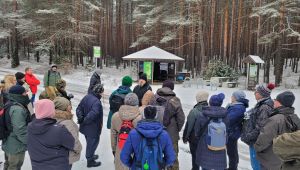 Grupa kilkudziesięciu osób strojąca w ośnieżonym lesie i słuchająca wypowiadającego się Pana Mirosława Worony - przewodnika...