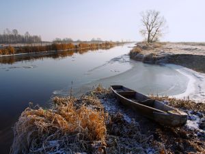 Biebrza zimą - koryto rzeki a w pierwszym planie łódź drewniana na brzegu.
